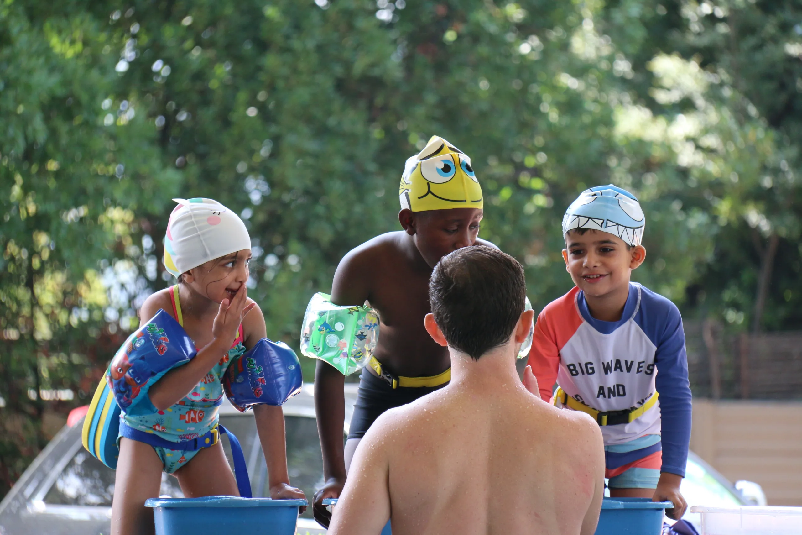 Happy children in colorful swim gear and floaties engaging with their instructor at Zogs Swim School. This fun outdoor swim lesson promotes water safety, confidence, and early swim skills in a nurturing environment.